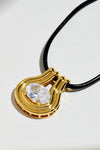 Gold pendant with a clear gemstone on a black cord against a white background