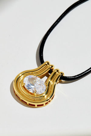 Gold pendant with a clear gemstone on a black cord against a white background