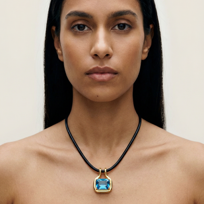 Woman wearing a necklace with a blue pendant against a neutral background
