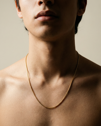 Close-up of a person wearing a gold necklace against a neutral background